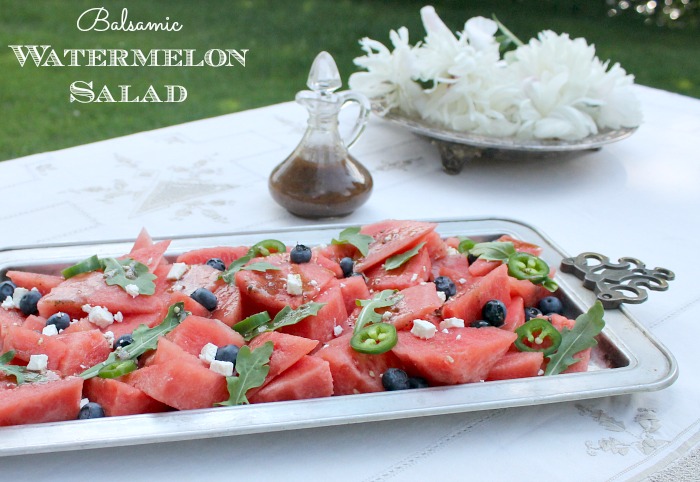A large platter of balsamic watermelon salad, next to a jug wil salad dressing on it