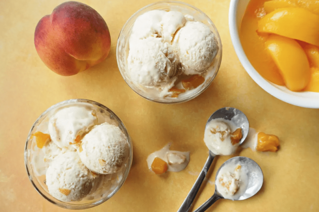 2 bowls filled with homemade peach ice cream, a bowl of sliced peaches, a whole peach and 2 spoons