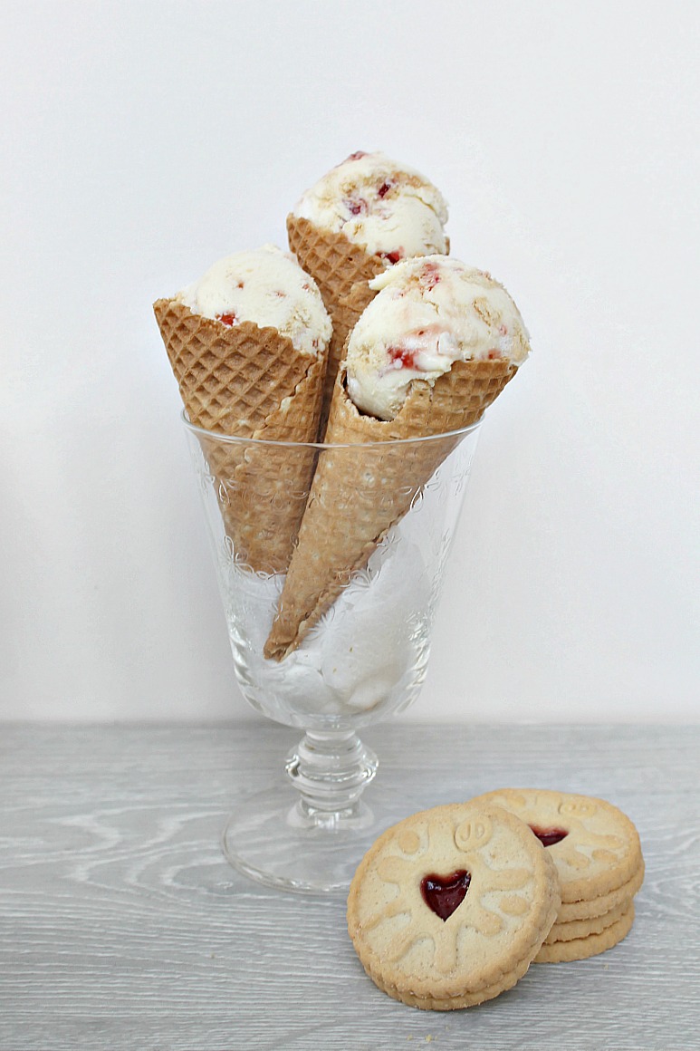 A glass containing three waffle cones with ice cream, with a stack of biscuits in front