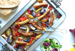 A baking tray with sausage, peppers, onions and potato