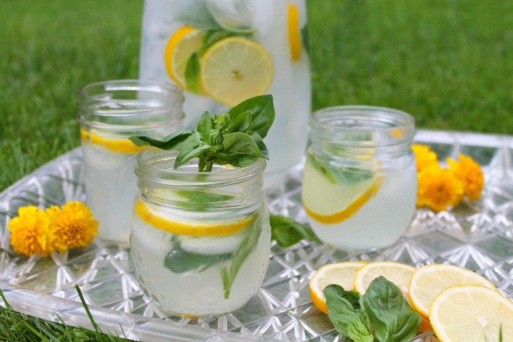 Gin Lemonade & Basil cocktail in jars and a jug, sat on a tray on the grass. The tray is decorated with lemons and basil