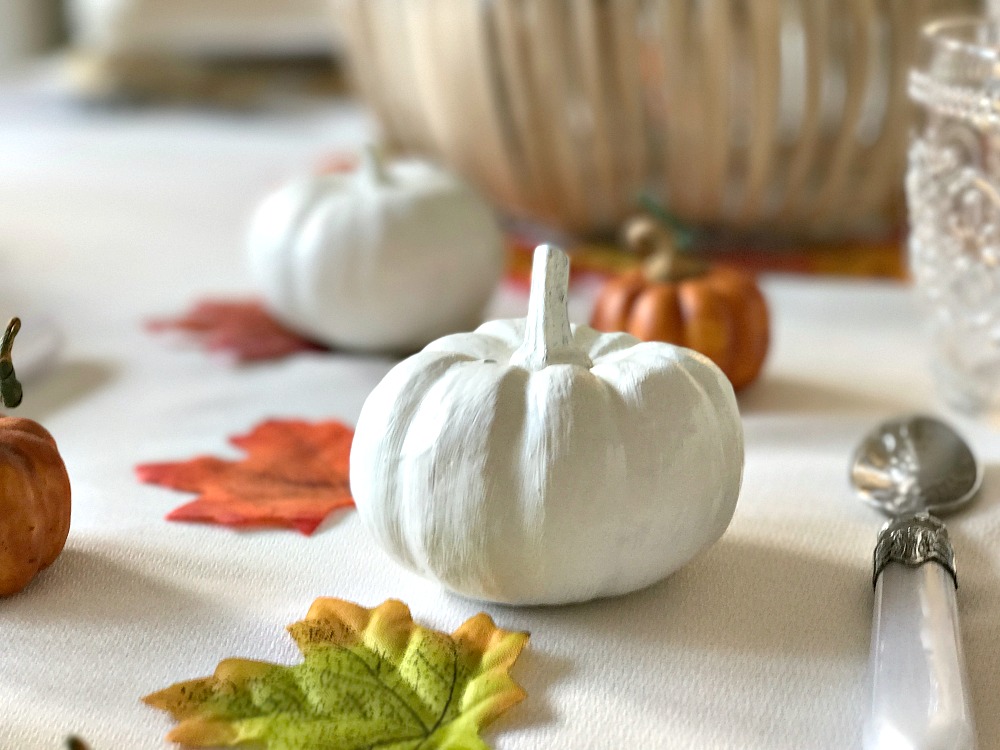 A painted white pumpkin on a table with fake leaves table settings