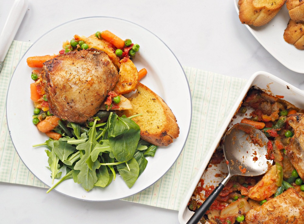 A plate with Rustic Chicken Casserole, mixed vegetables, garlic bread and a leaf salad.