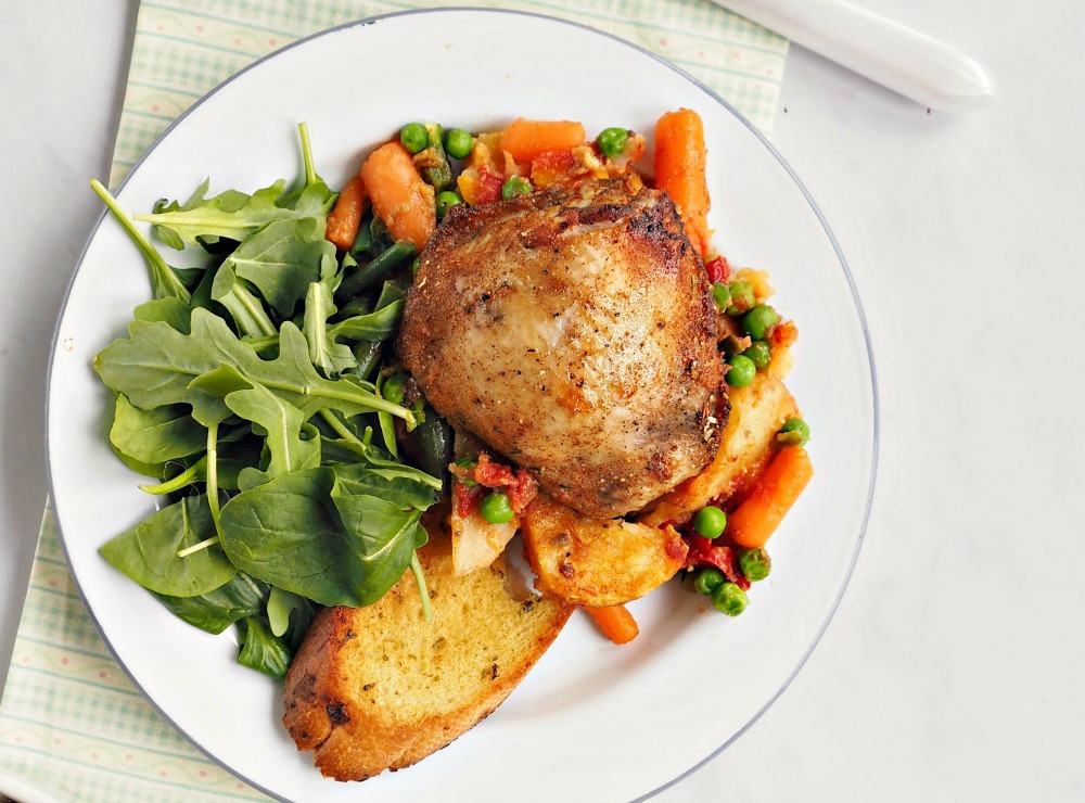 A plate with Rustic Chicken Casserole, mixed vegetables, garlic bread and a leaf salad.