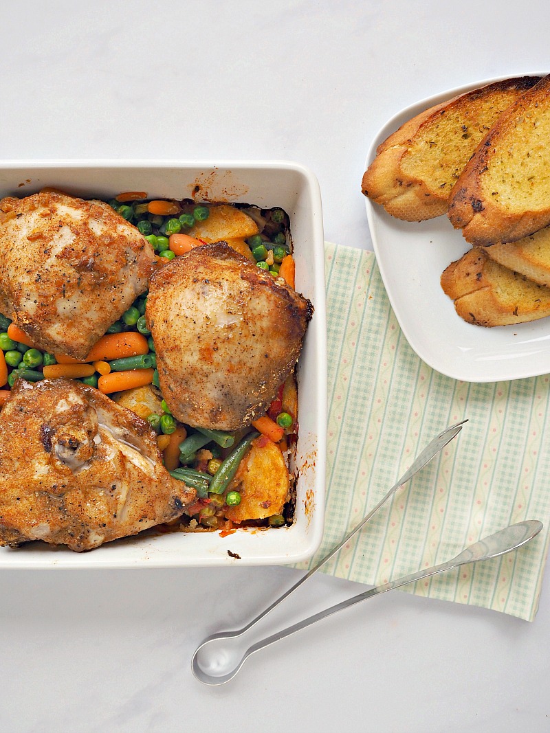 A large dish containing chicken and mixed vegetables, and a separate place with garlic bread.