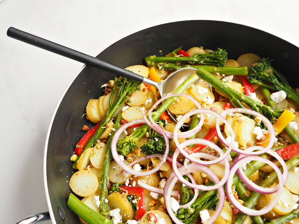 A frying pan containing Lime and Chilli Potatoes with onion, peppers and tenderstem broccoli.