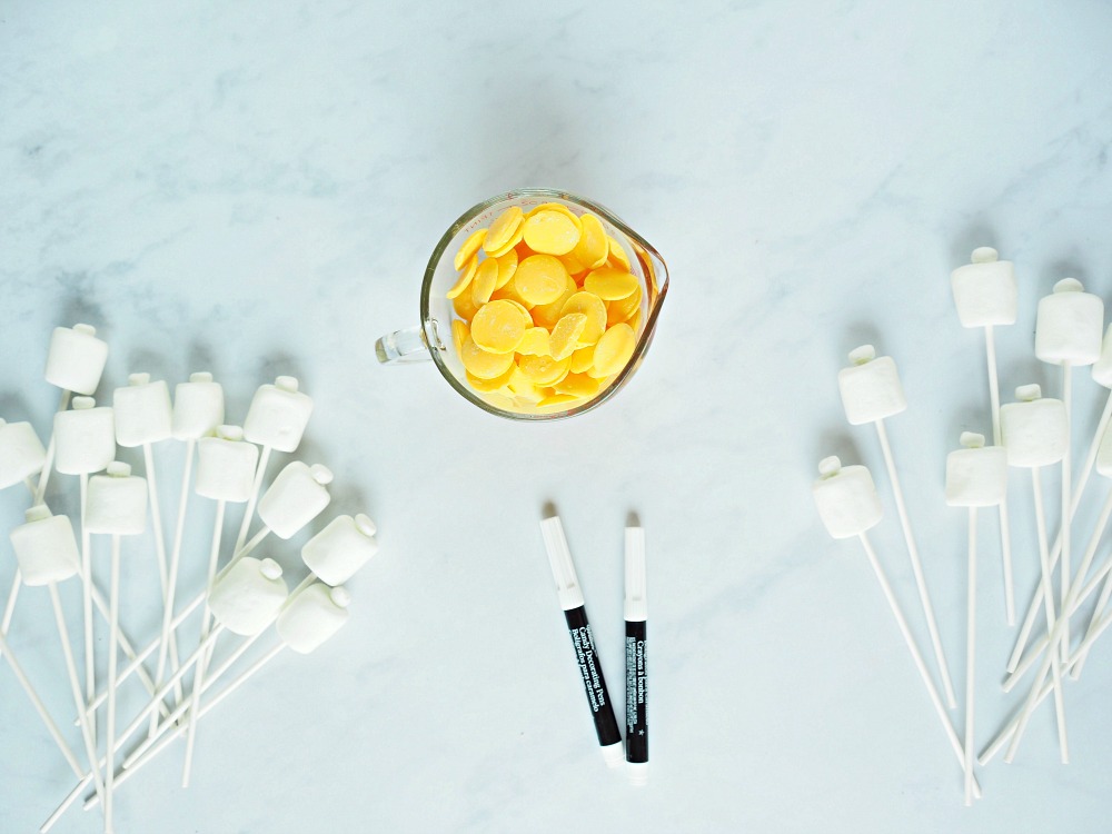White marshmallow pops lie on either side of a jug containing yellow chocolate dots
