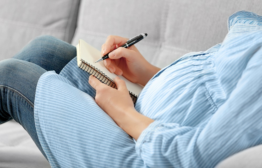 a pregnant women in maternity clothes lying on a sofa with a notebook and pen