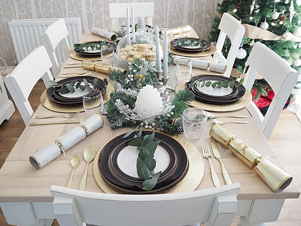 A table set for Christmas dinner in a rustic theme with gold and white accents