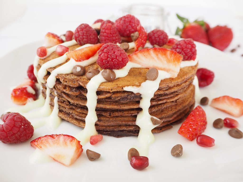 A stack of chocolate pancakes, topped with a cream cheese glaze, strawberries, raspberries and chocolate chips