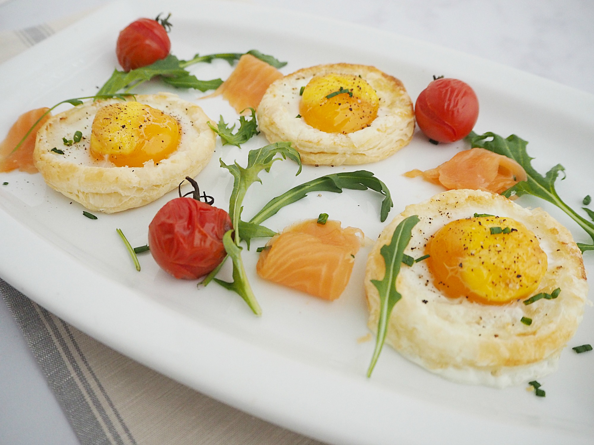 A plate of baked eggs, smoked salmon, rocket and roasted cherry tomatoes