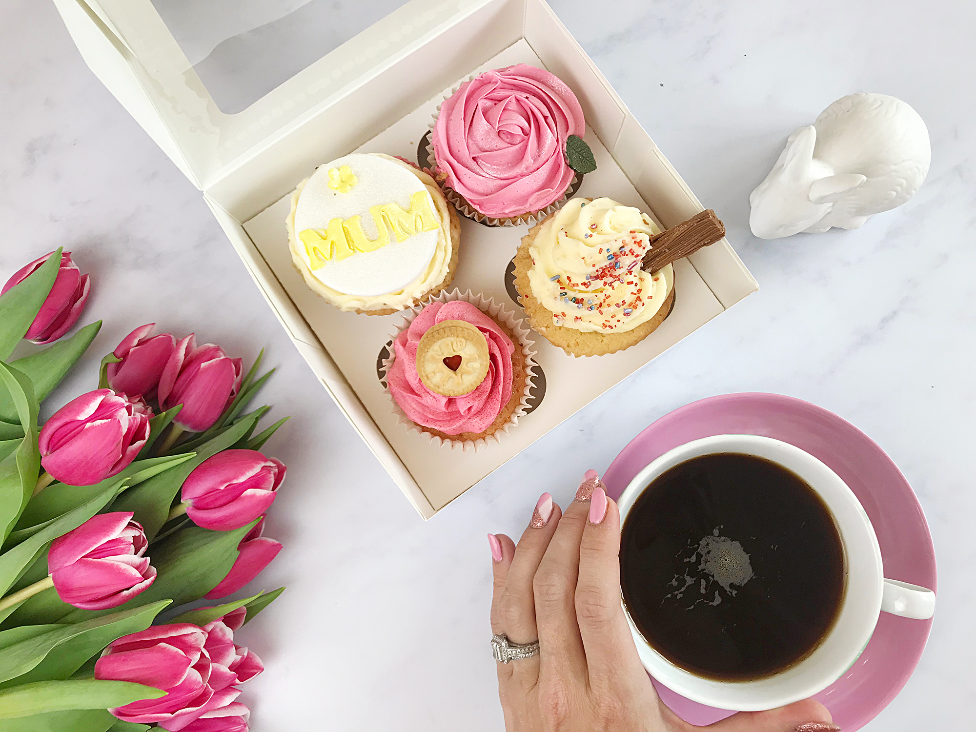 4 cupcakes in a box next to a bouquet of tulips and a cup of coffee