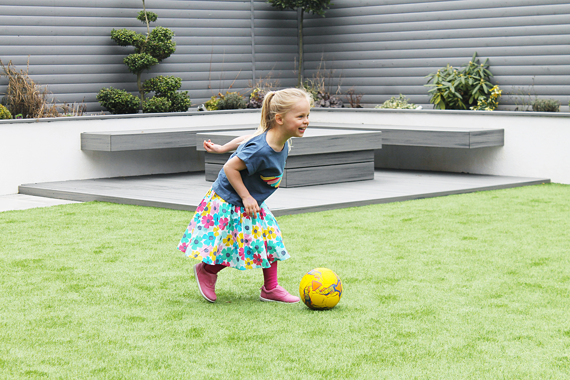 A girls in a skirt and t-shirt playing in a garden with a football