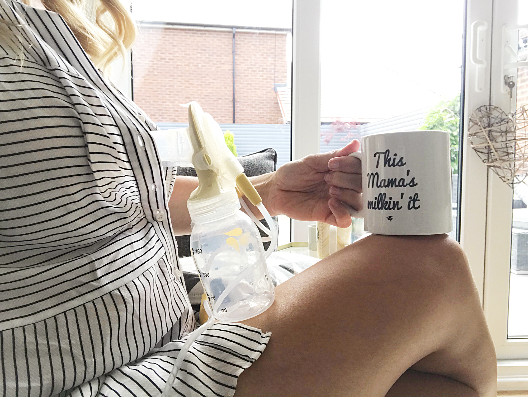 A woman in a black and white striped dress sitting with a breast pump and a mug with "This mama's milkin' it" on it