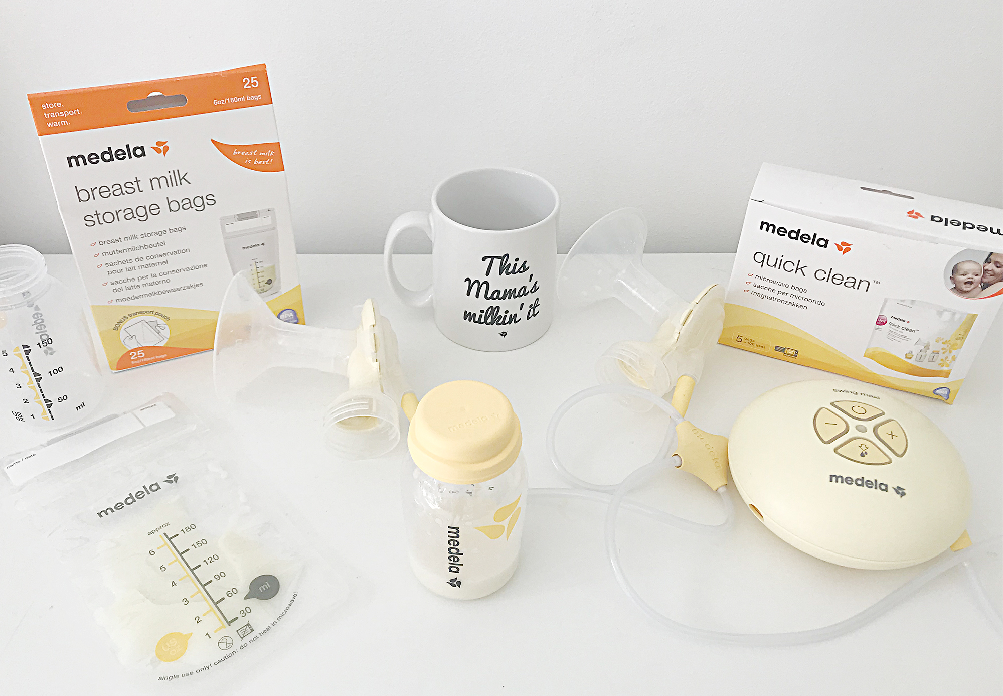 A white table with a box of breast milk storage bags, a breast pump, a mug and some breast milk storage bags on it