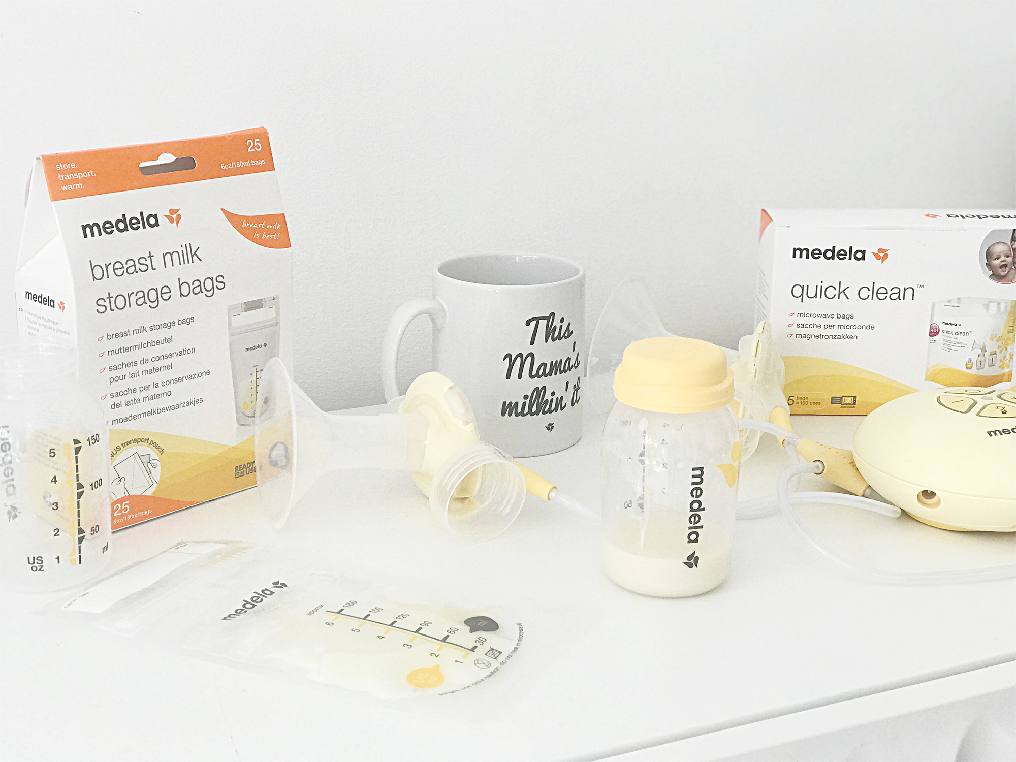 A breast pump, milk storage bags and a mug on a white table