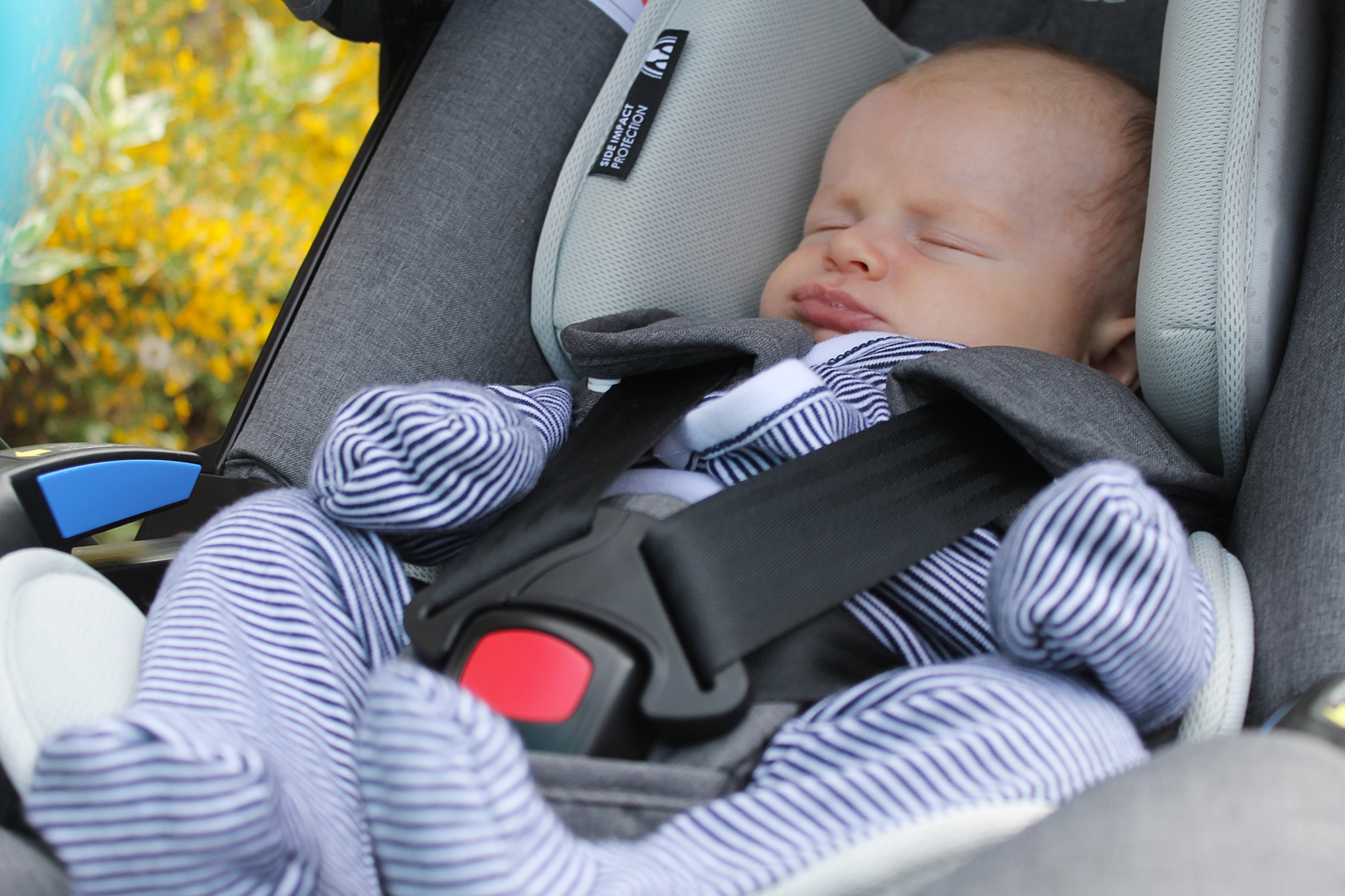 A baby in a striped sleep suit asleep in a car seat