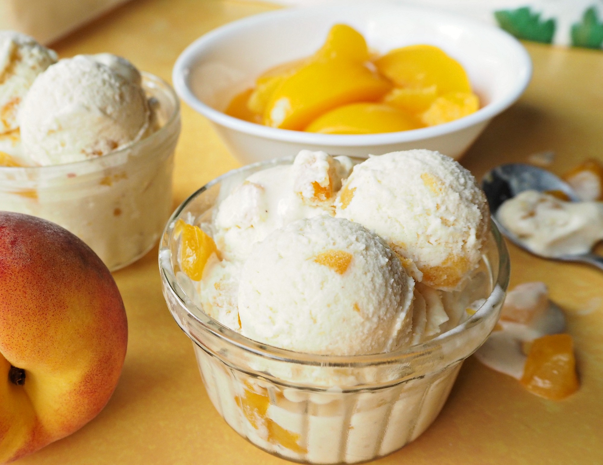 Bowls of peach ice cream next to a bowl of sliced peaches.