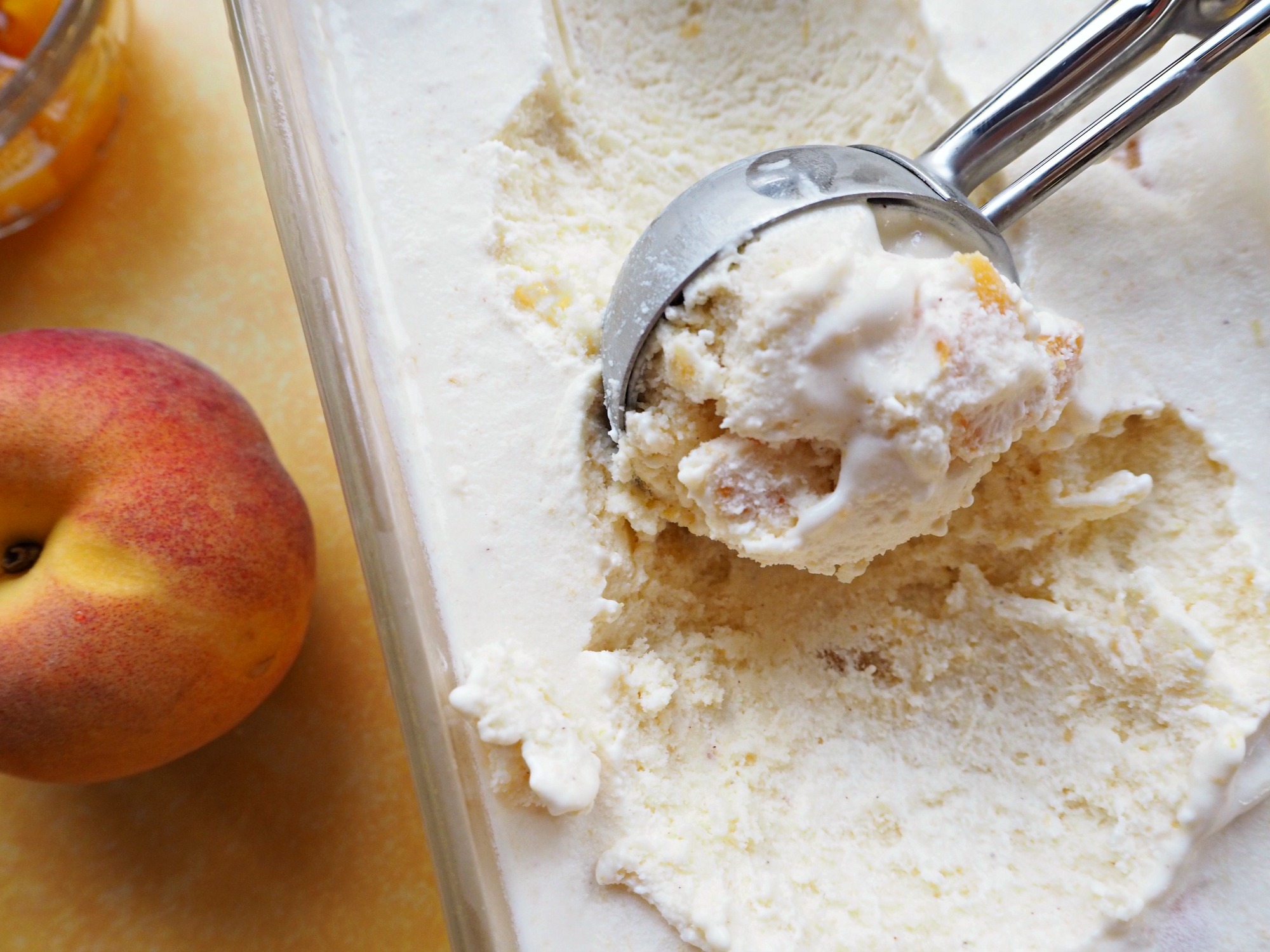 An ice cream scoop in a tub of homemade peach ice cream