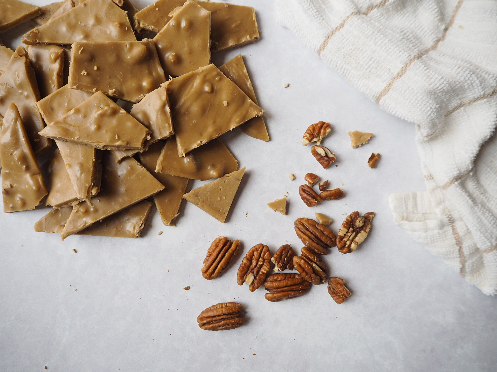 Caramel frosting bites next to some pecans and a cream coloured dish towel