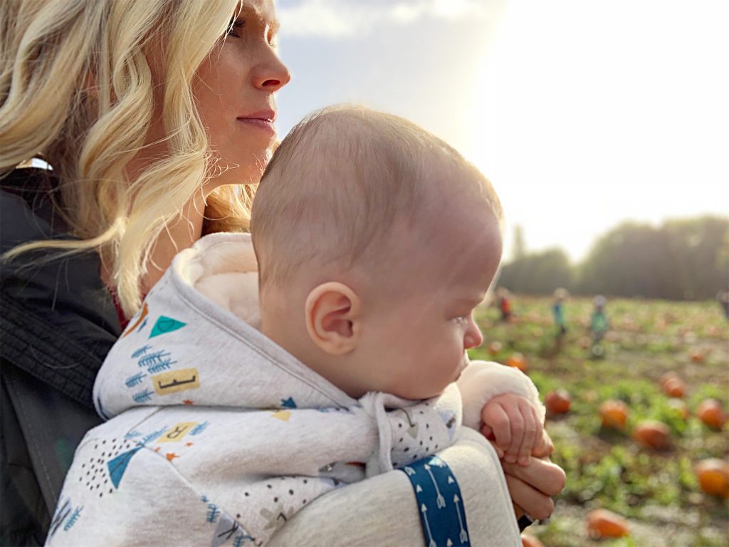 A blonde women holds a baby and looks out over the pumpkin patch