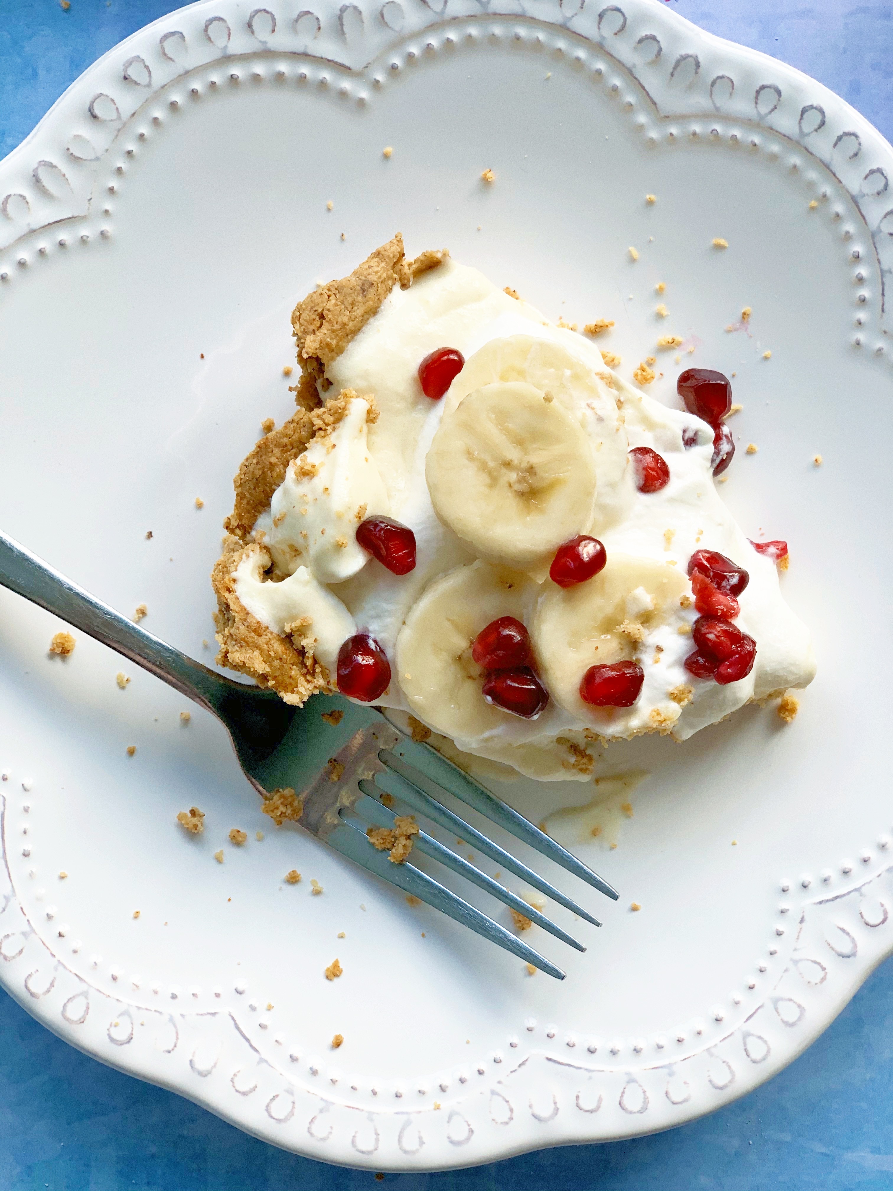 A slice of Vegan Banana Cream Pie with Pomegranate on a white plate with a fork.