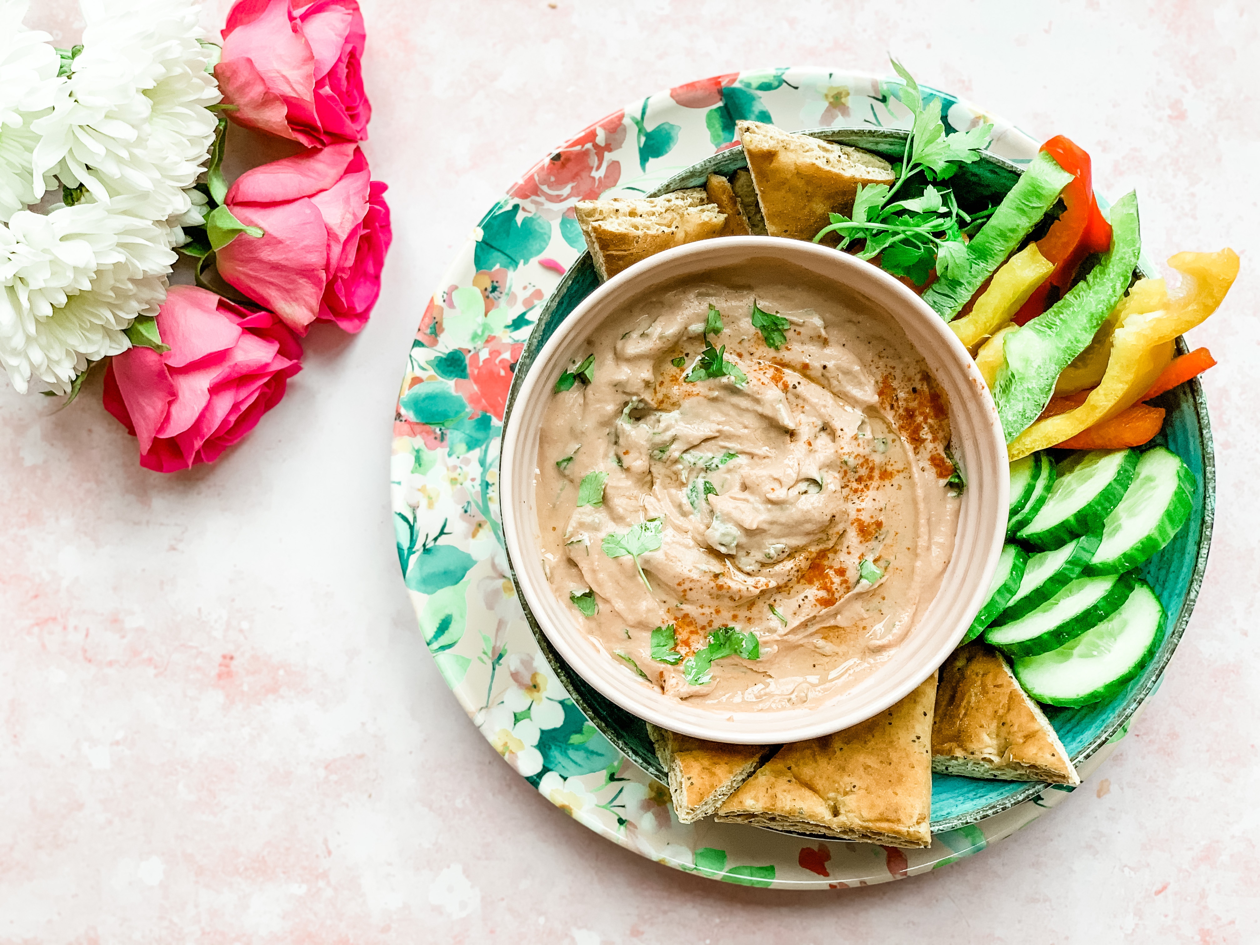 A bowl of baba ganoush, drizzled with olive oil and paprika. It sits surrounded by chopped vegetables and bread.