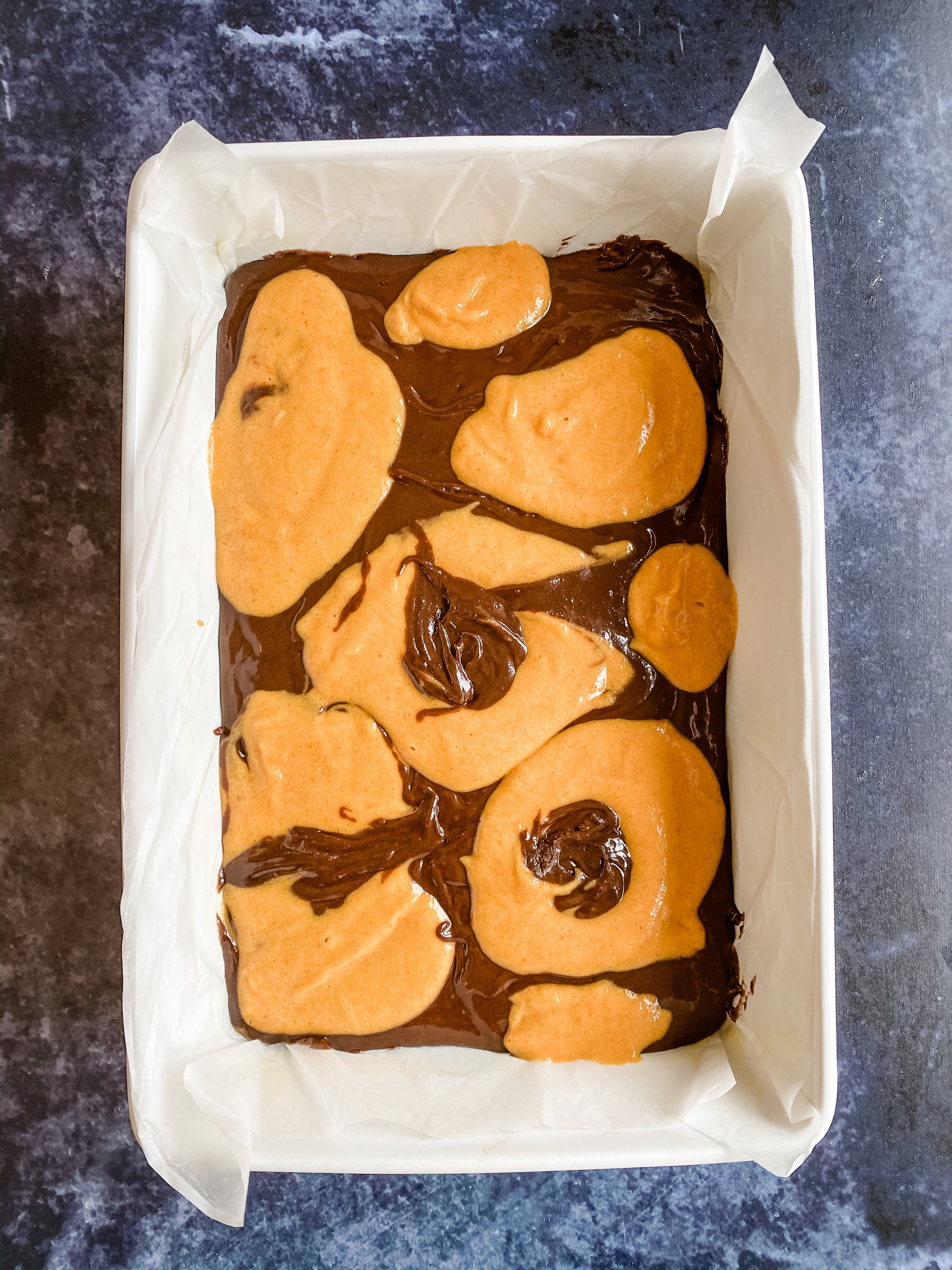 A tray of brownie and pumpkin mixture before it is swirled and baked