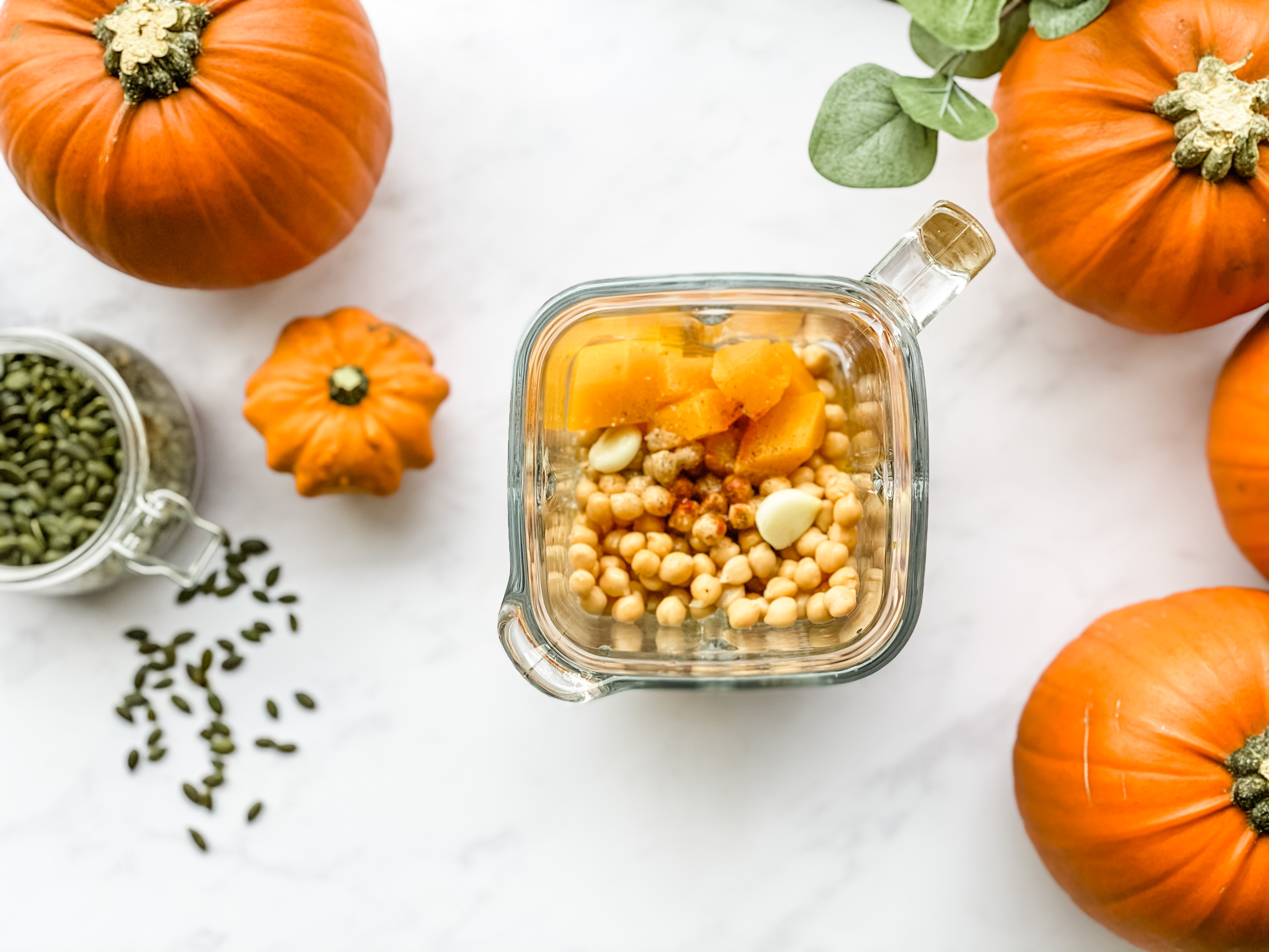 A glass blender filled with pumpkin, garlic, spices and chickpeas