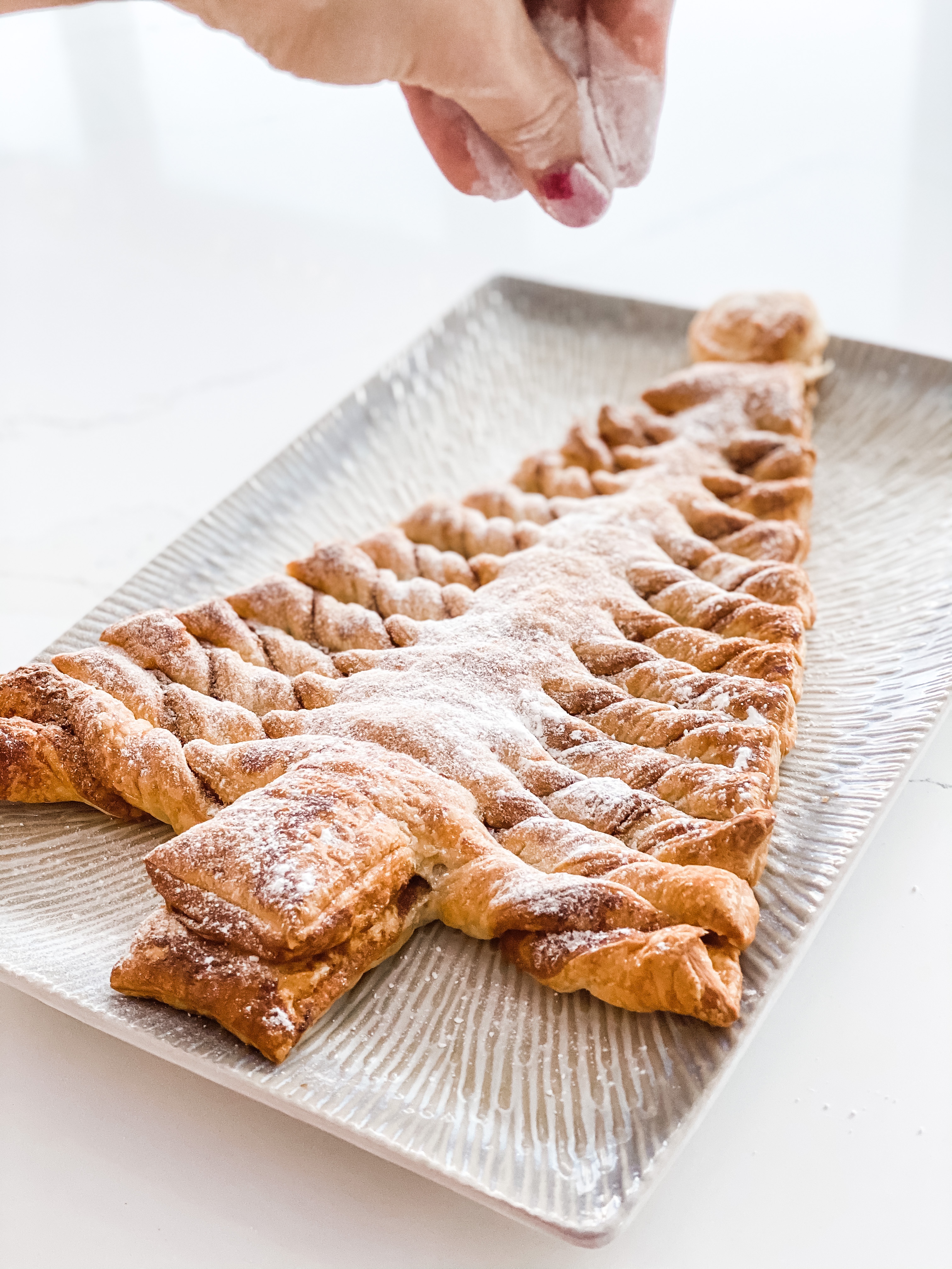 A puff pastry Christmas tree being sprinkled with icing sugar
