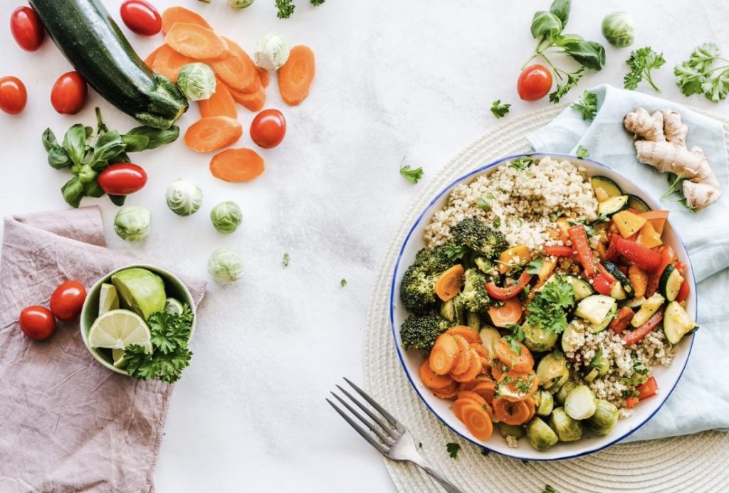 A bowl full of vegetables and rice. On the table are scattered more vegetables