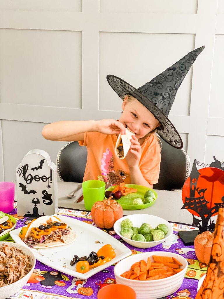 A girl in a witches hat biting into a taco