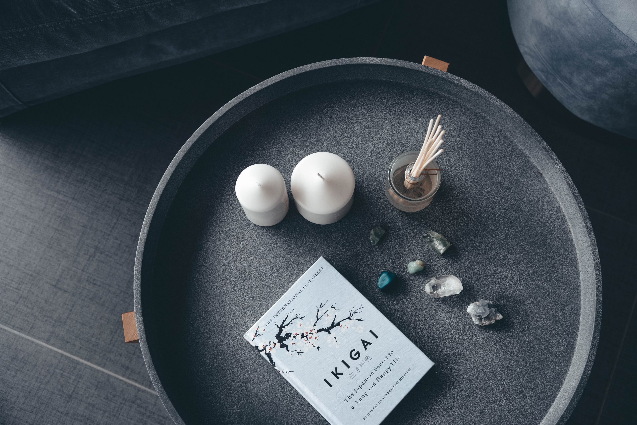 A large black tray with some white candles, a reed diffuser and a book on it