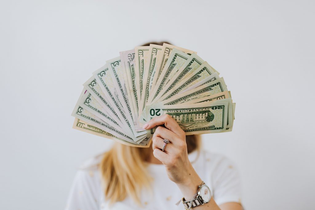 A person wearing a white tshirt holding up a stack of dollars like a fan