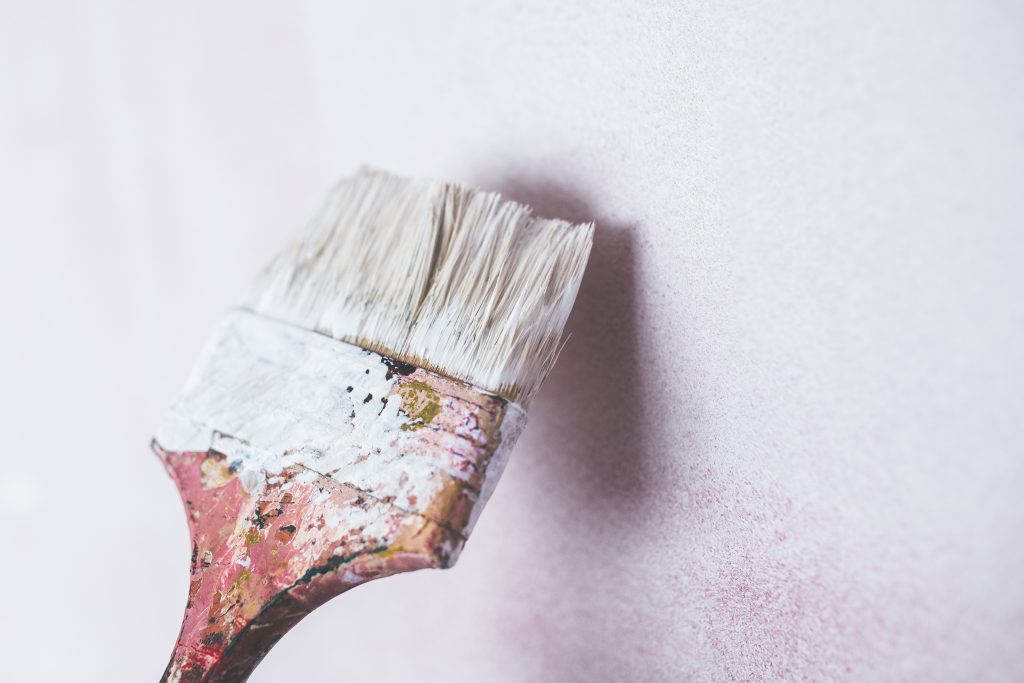 An old worn paint brush with white paint on it against a white wall