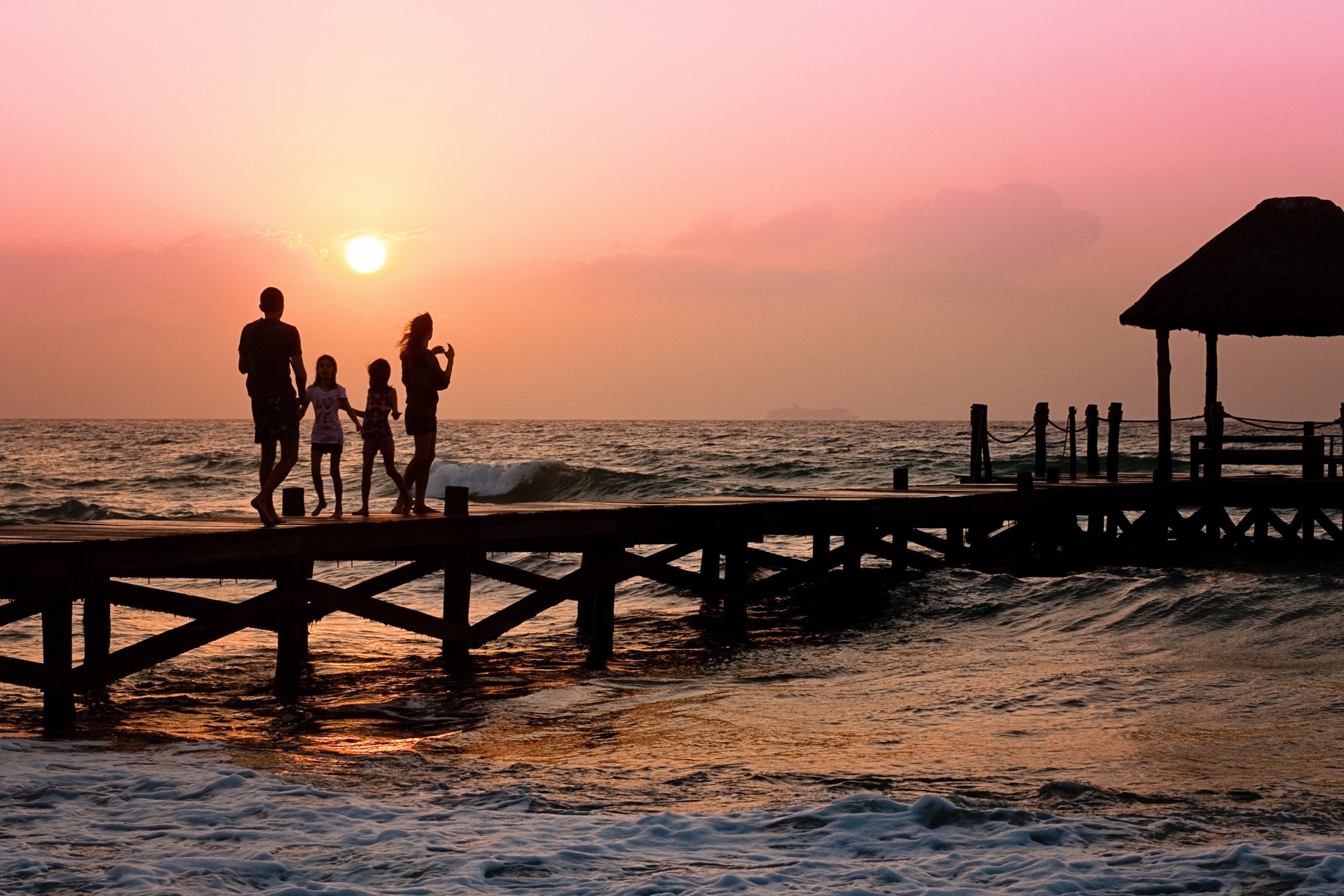A silhouette of a family standing on a jetty at sunset