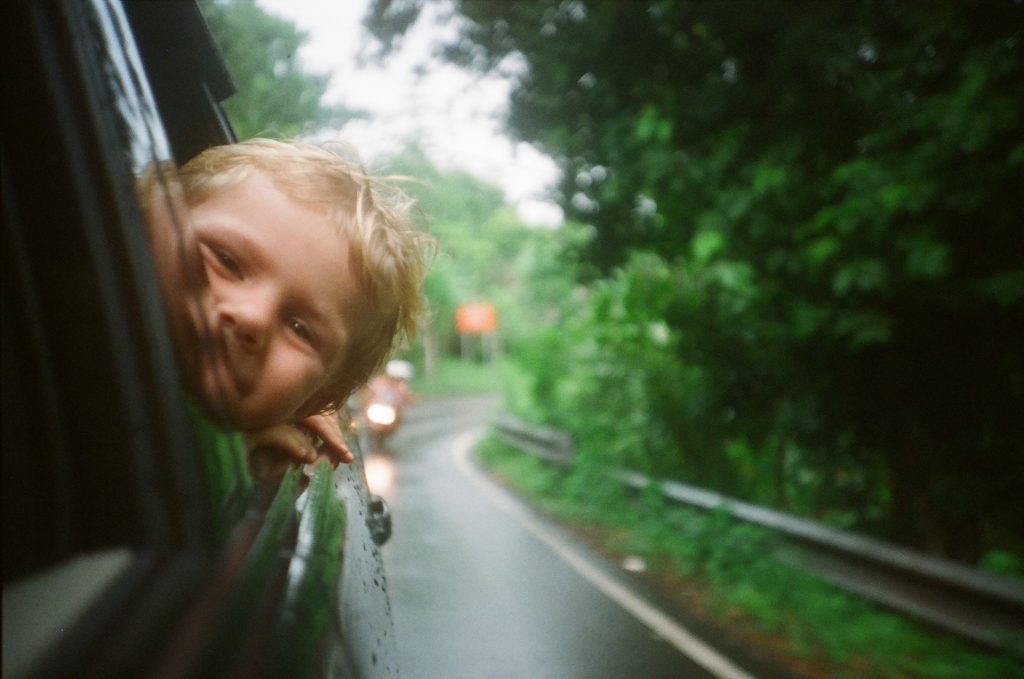 A child poking their head out of a car window.
