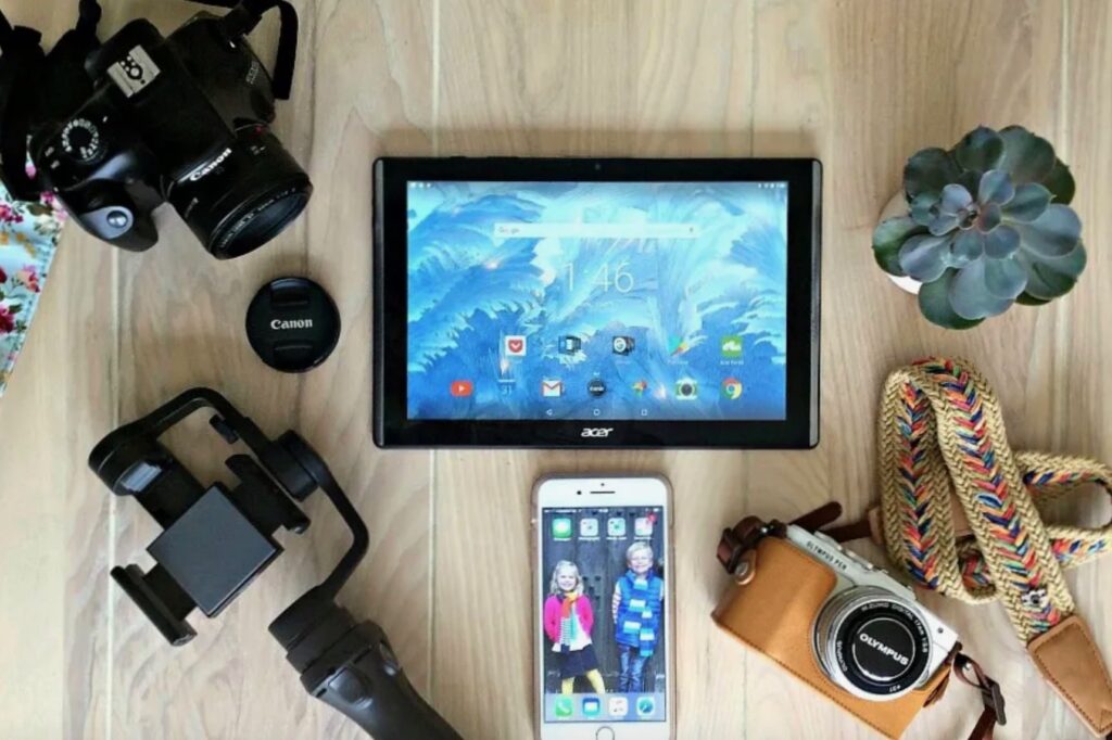 A camera, phone, tablet and other electrical items laid on a wooden floor