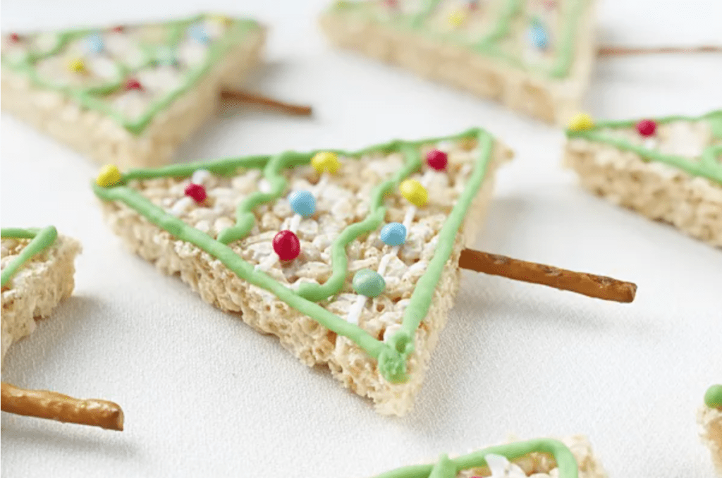 A rice krispy tree in a triangle shape with a pretzel stick stuck in the bottom. It is decorated with icing to make it look like a Christmas tree