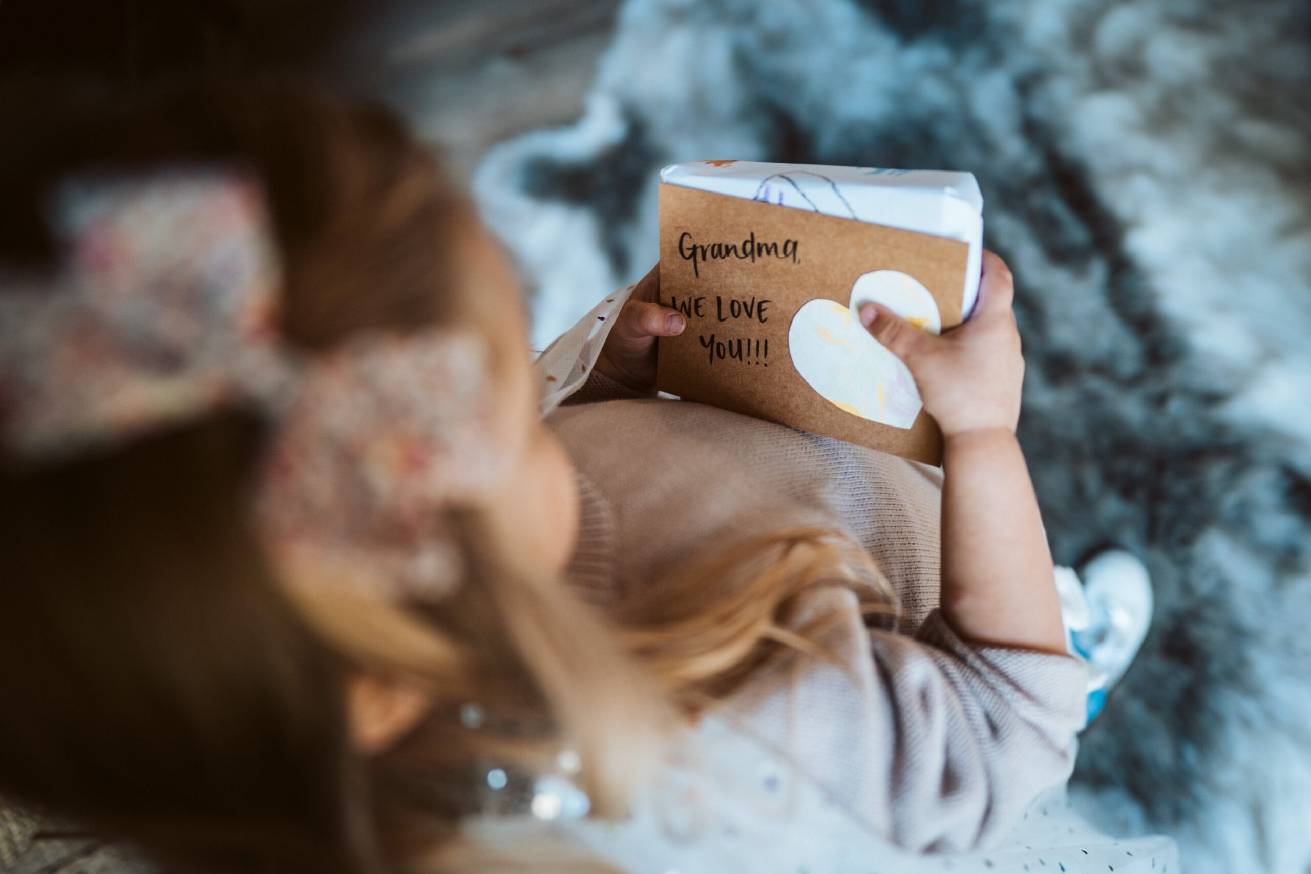 A girl hosing a small present with a brown label with "Grandma we love you!" written on it
