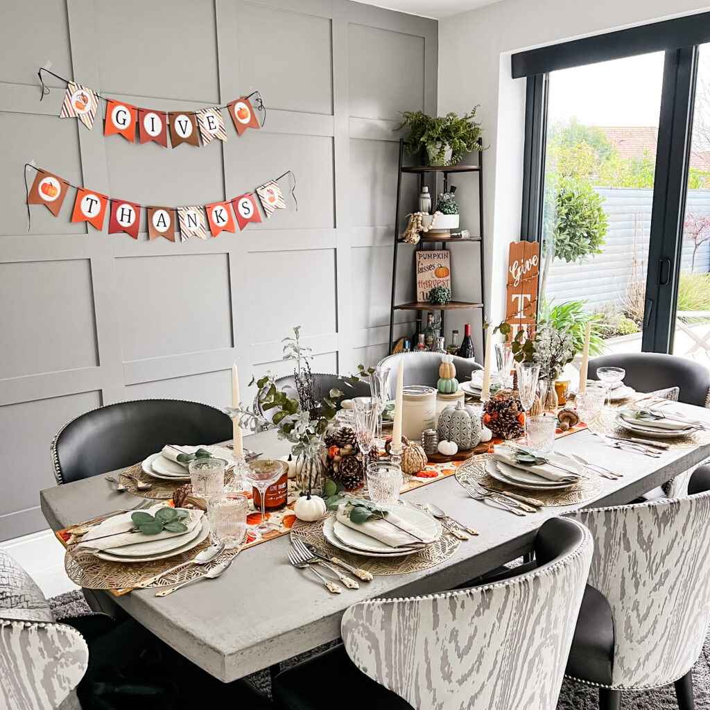 a holiday tablescape for Thanksgiving. The table is set for dinner and decorated with pumpkins and pinecones and candles