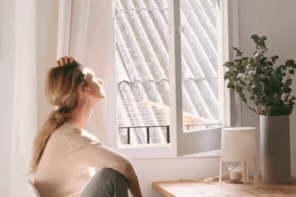 A woman sitting and looking out of a window in a bright room