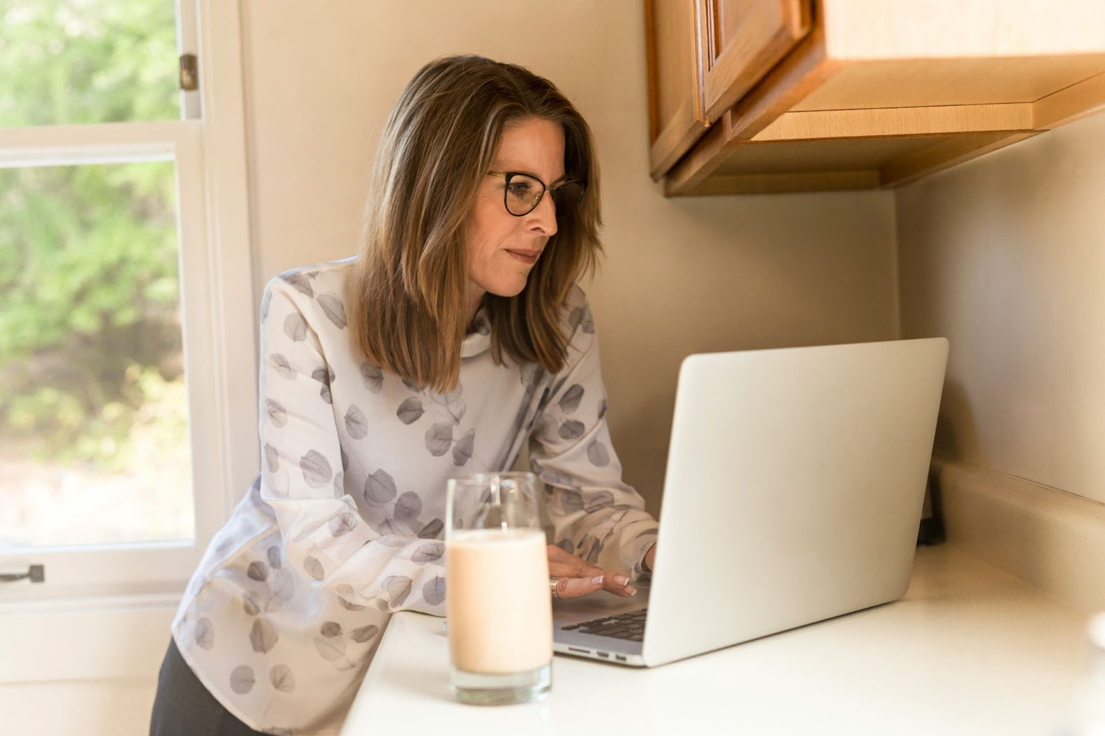 A woman standing at a counter and typing on her laptop