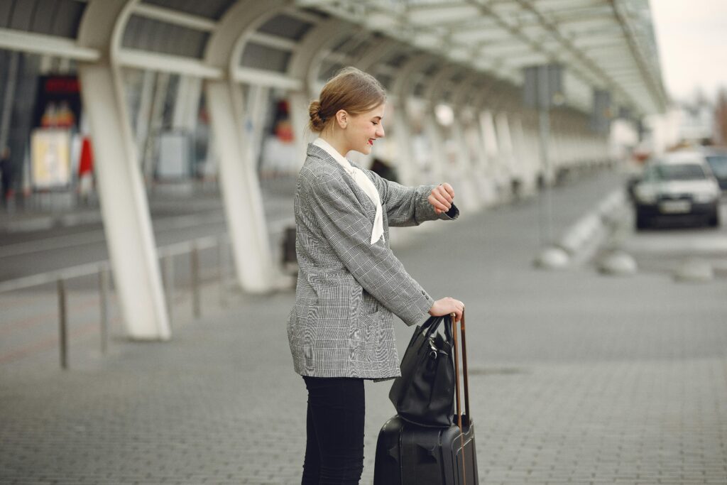 A woman, looking at her watch, is holding a suitcase in preparation for her next trip abroad.