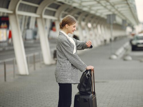 A woman, looking at her watch, is holding a suitcase in preparation for her next trip abroad.