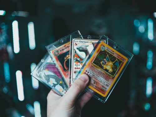 A child holding up several pokemon cards as gift ideas against a dark background.