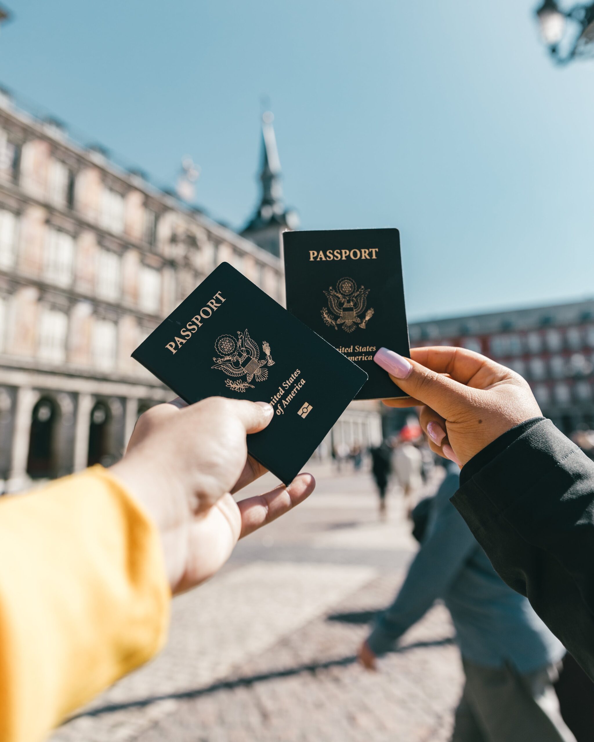 Two people holding passports in front of a building, discussing their EB-2 NIW Visa applications and the US Job Market.