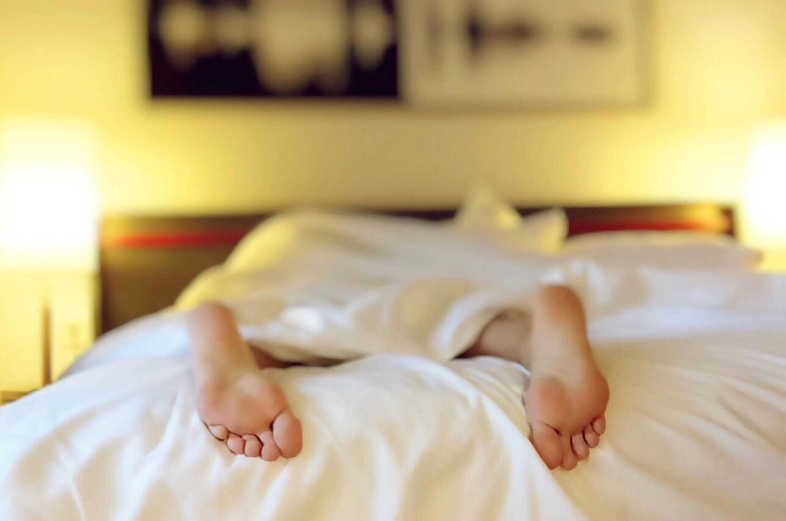 A person's feet are fixing in a bed with white sheets, going through their sleep cycle while feeling depressed.
