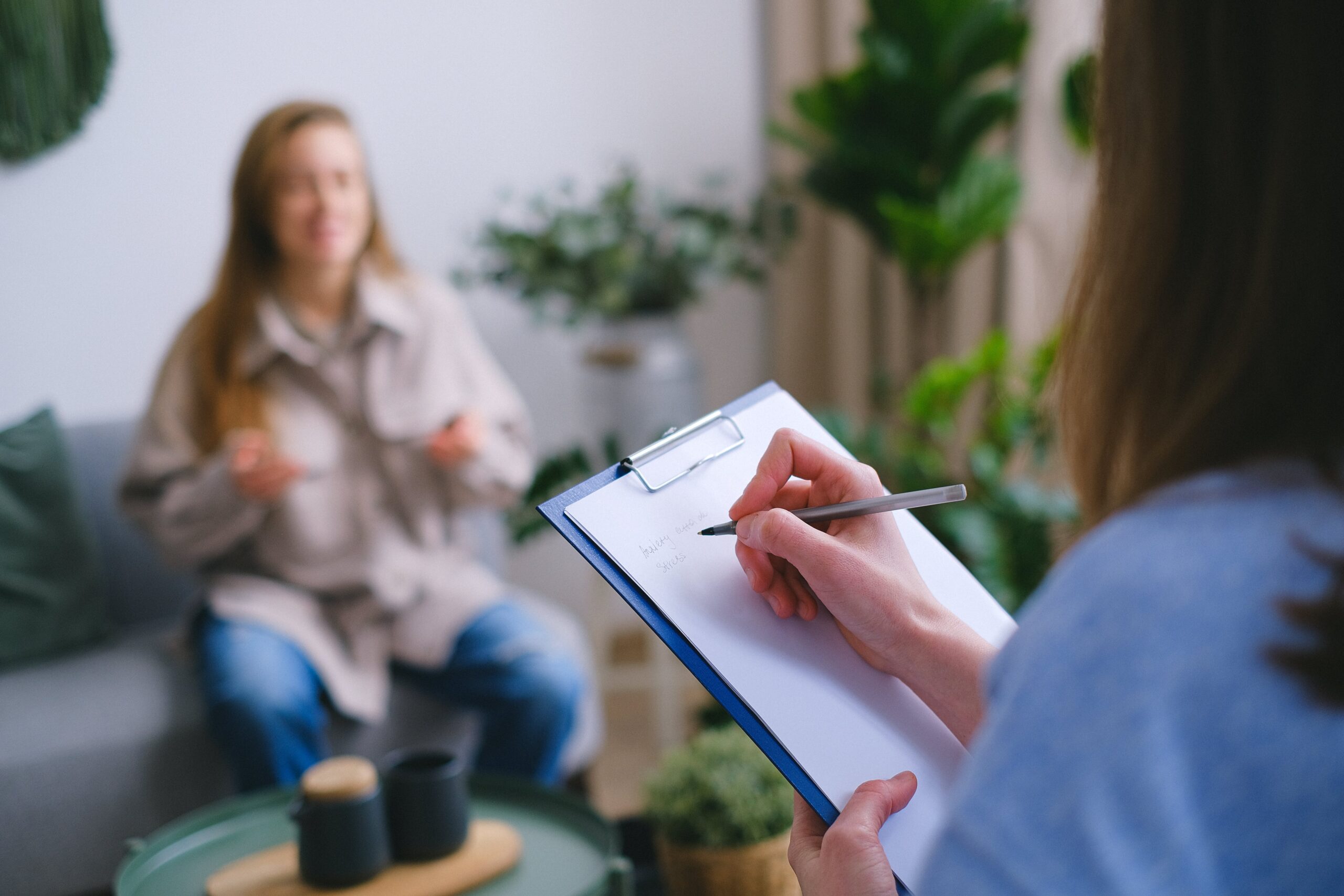 A therapist is sitting on a couch with a clipboard in front of her.