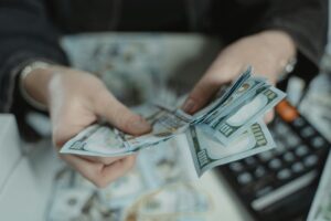 A person is holding a stack of money while calculating expenses.